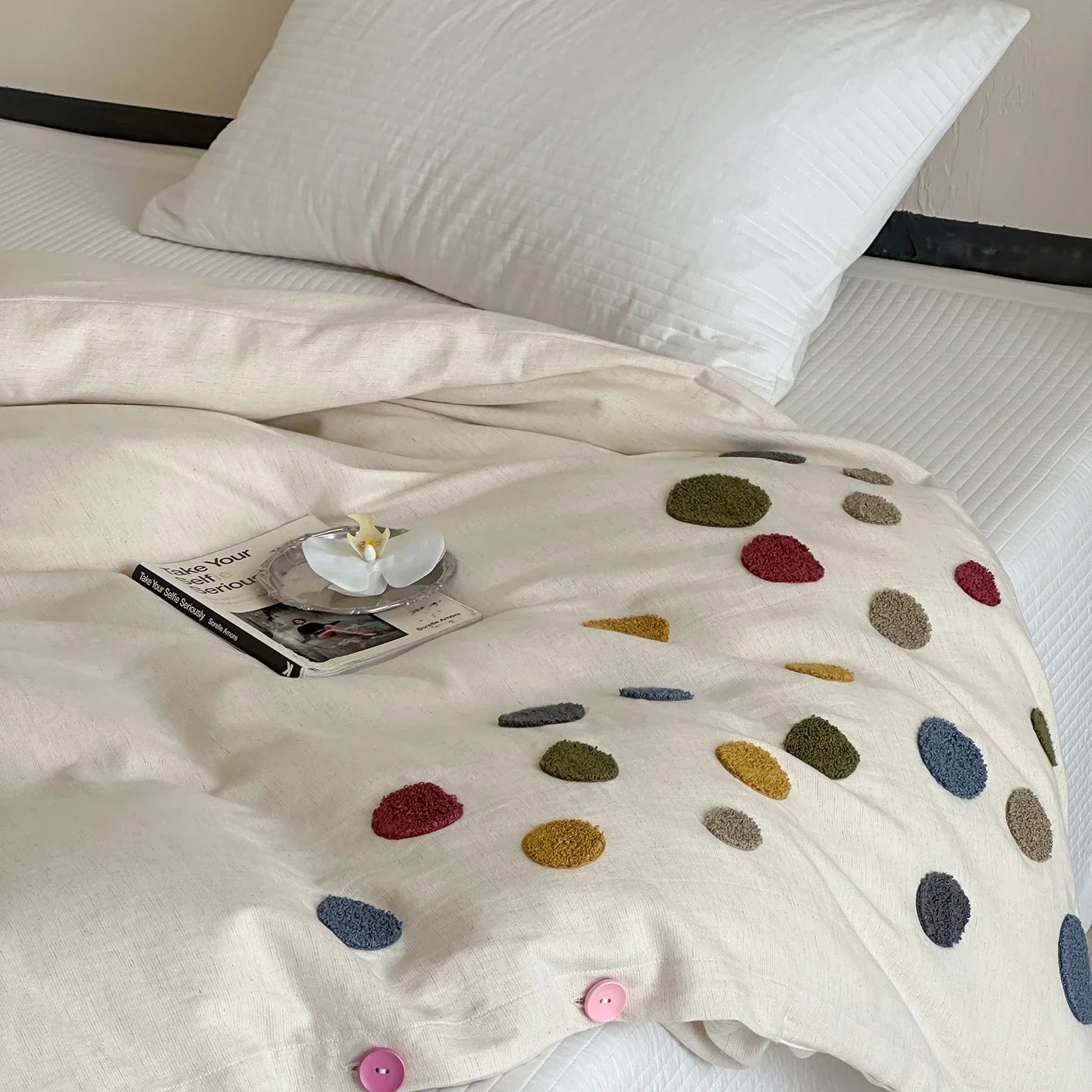 Beige duvet cover with colorful textured dots on a bed, styled with a pillow and a book.
