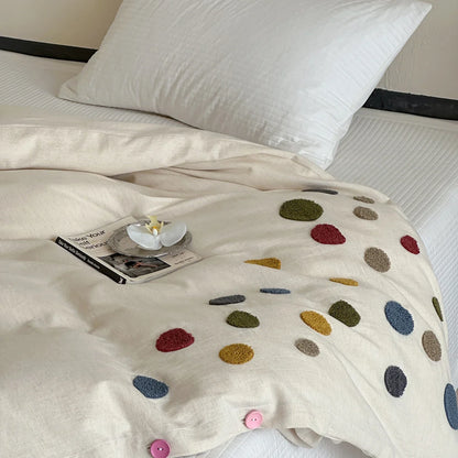 Beige duvet cover with colorful textured dots on a bed, styled with a pillow and a book.